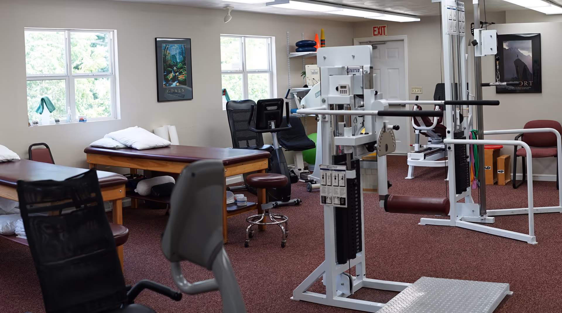 A spacious physical therapy room with tables, exercise equipment, and chairs.