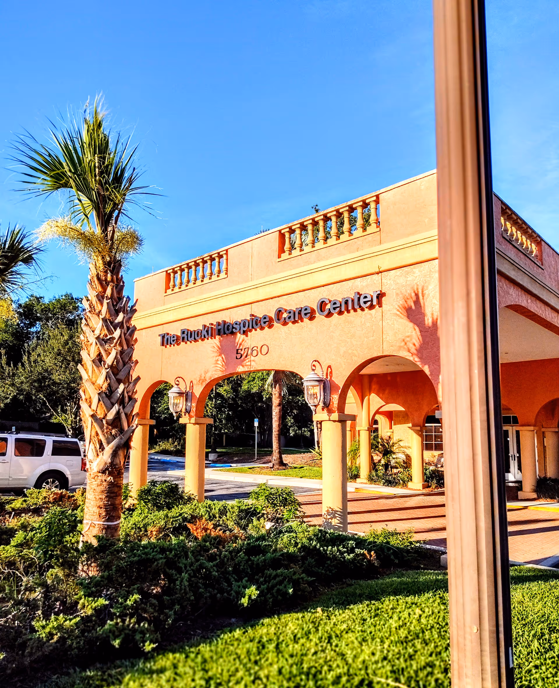 Exterior view of a peach-colored building with arches and palm trees under a blue sky.