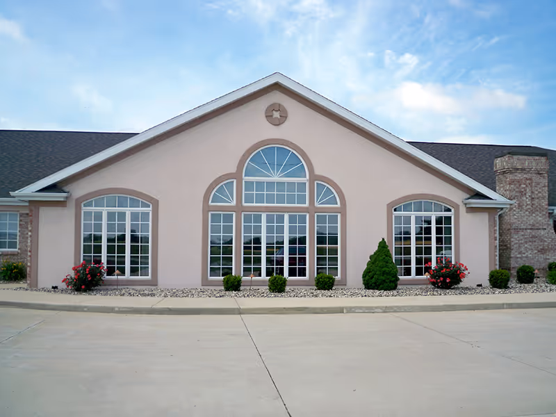 Front exterior of a single-story building with three large arched multi-pane windows, landscaping and a paved driveway.