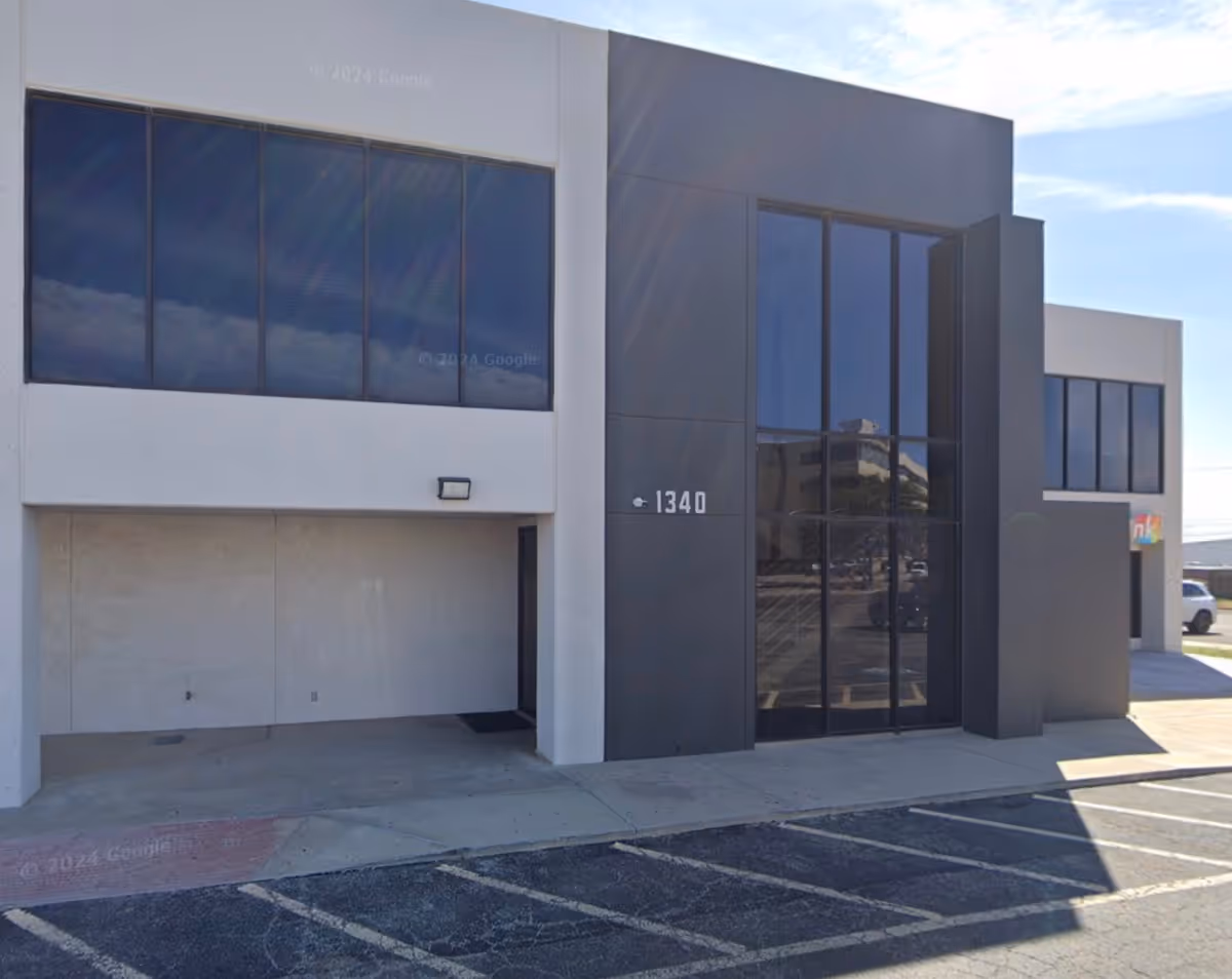 Exterior view of a modern building with large glass entrance and parking lot.