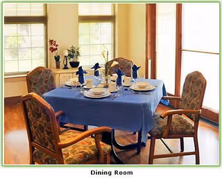 A dining room with a blue tablecloth, four upholstered chairs, and place settings.