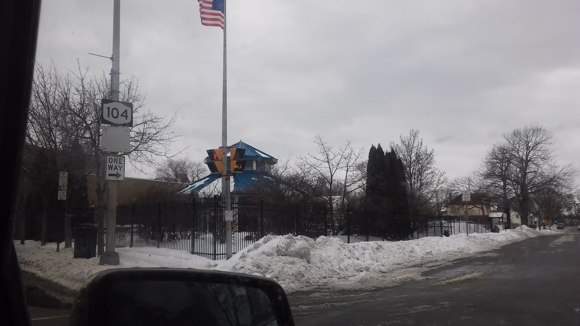 Snowy street view of a fenced senior care facility with a blue-roofed pavilion and flag.