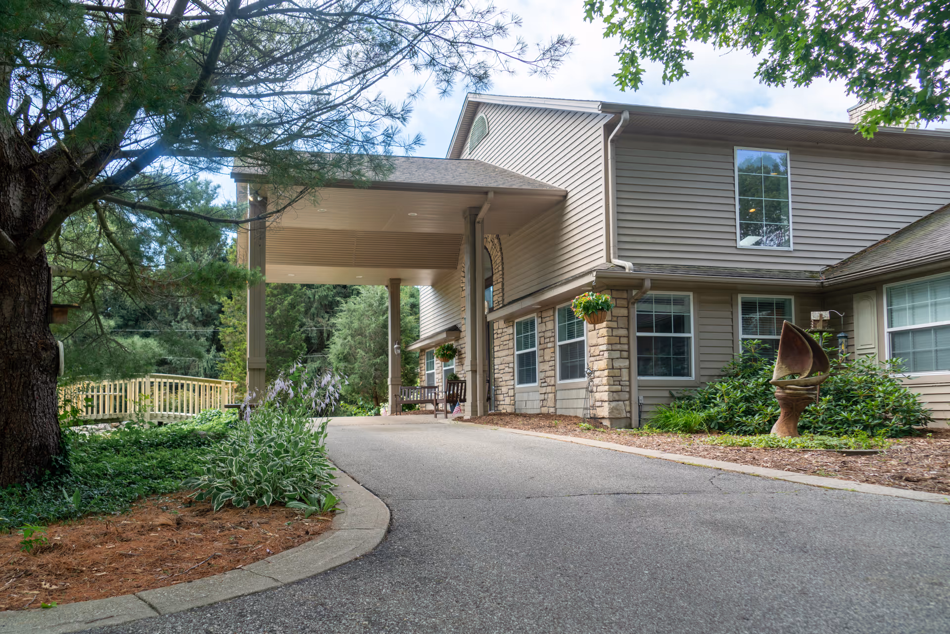 Covered driveway and entrance of a two-story residential building with landscaping and hanging plants.