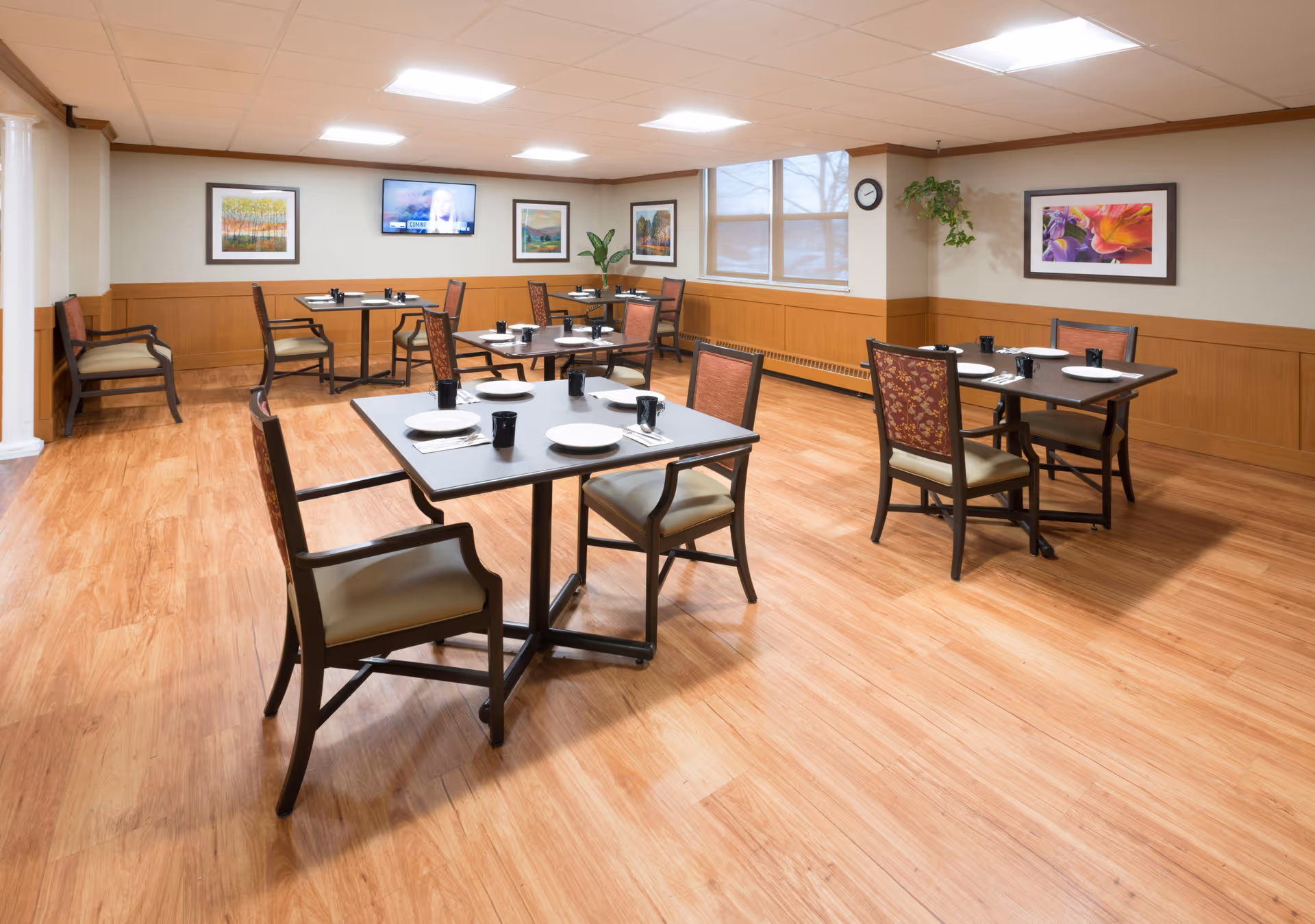 Spacious dining room in a senior facility with multiple tables, chairs, and place settings.