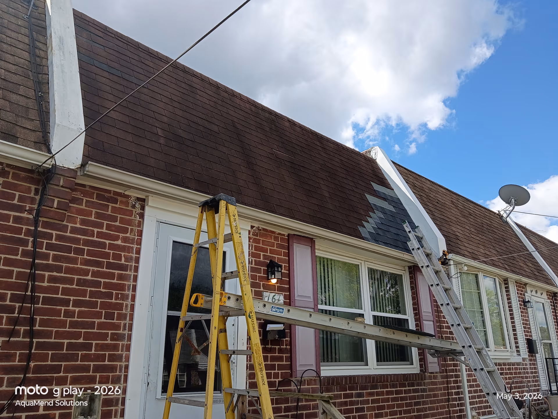 Brick house exterior with ladders and ongoing roof work under a blue sky.