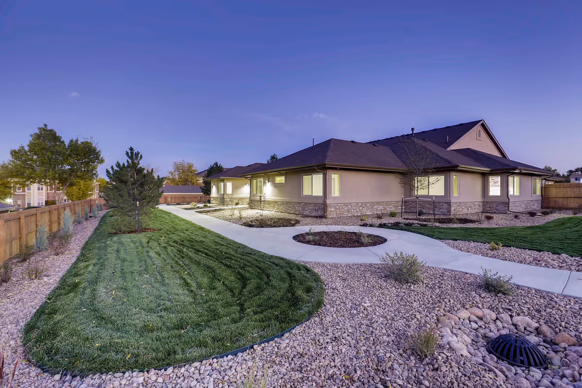 Single-story assisted living facility with curved walkway, gravel landscaping, and manicured lawn.