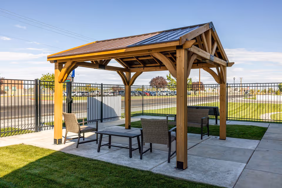 Wooden gazebo pavilion with outdoor seating in a fenced courtyard.