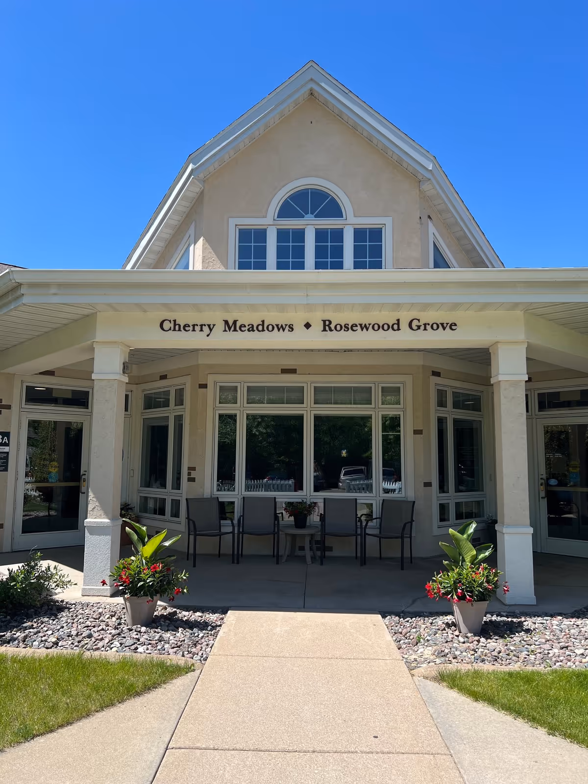 Front view of Cherry Meadows Rosewood Grove with porch seating and potted plants.