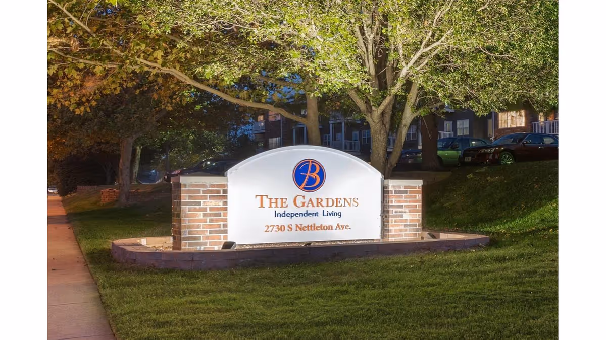 Front sign for The Gardens Independent Living with brick pillars and trees.
