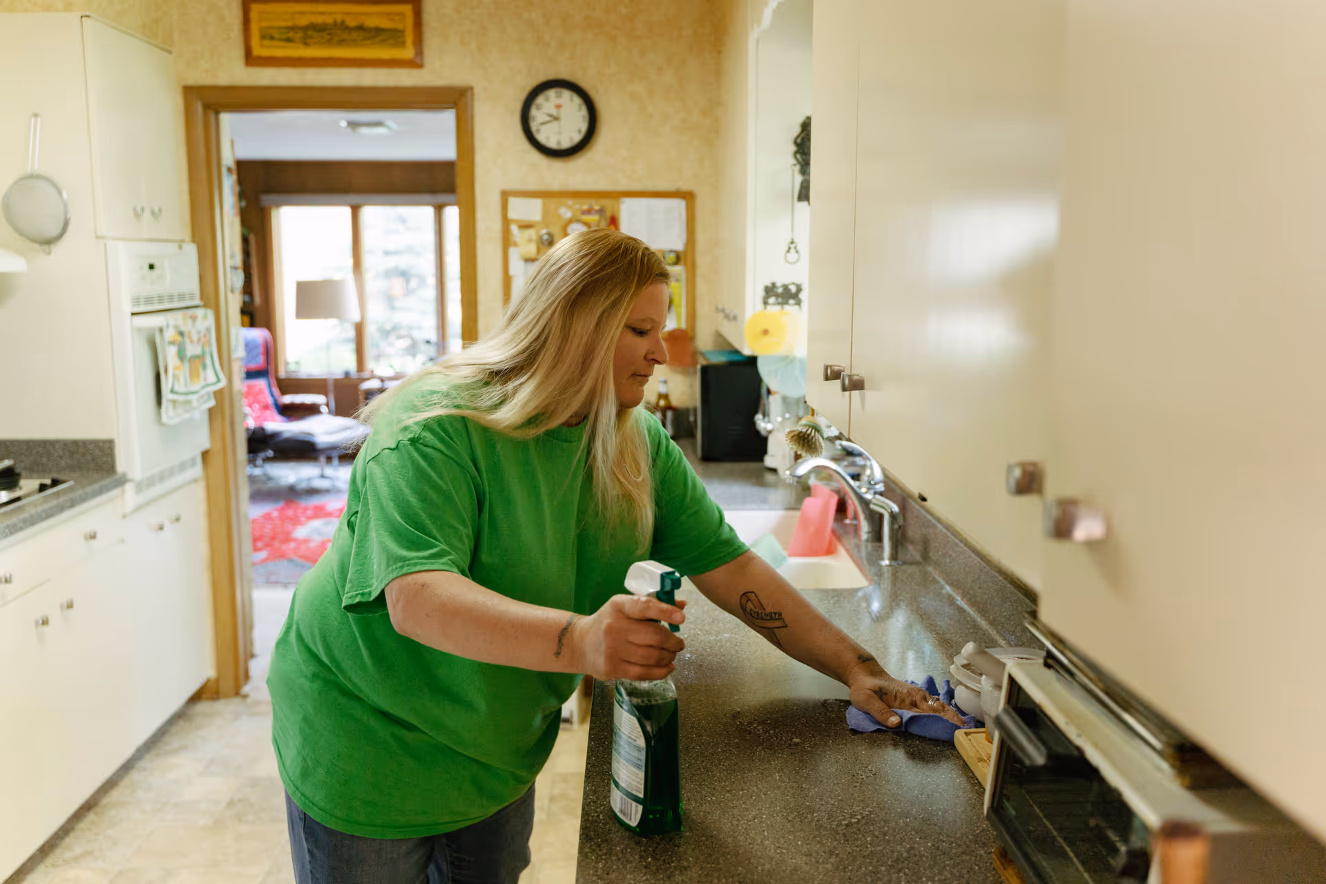 A woman in a green shirt cleans a kitchen counter in a senior living facility.