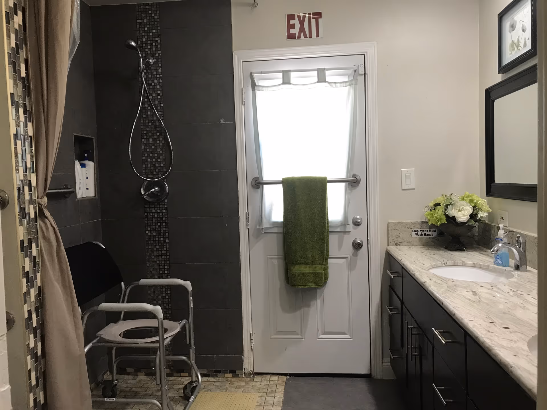 Bathroom in a senior living facility featuring a shower, chair, and marble countertop sink.