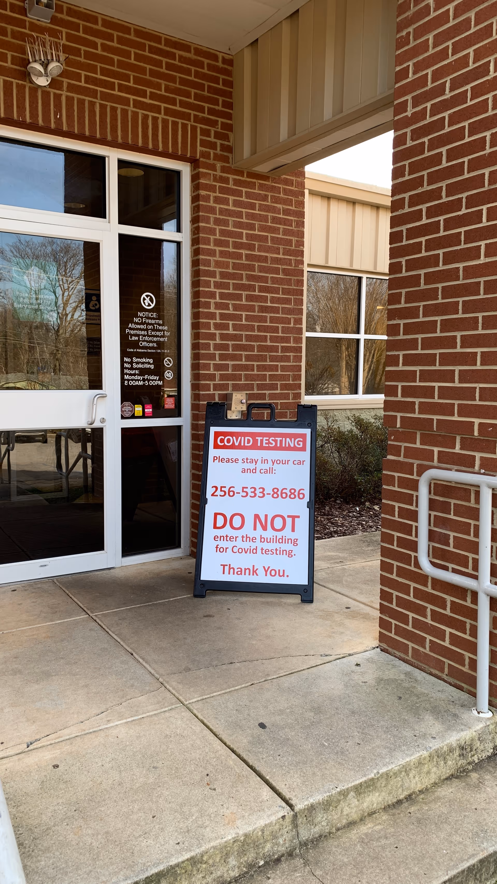 Brick building entrance with glass doors and a COVID testing sign outside.