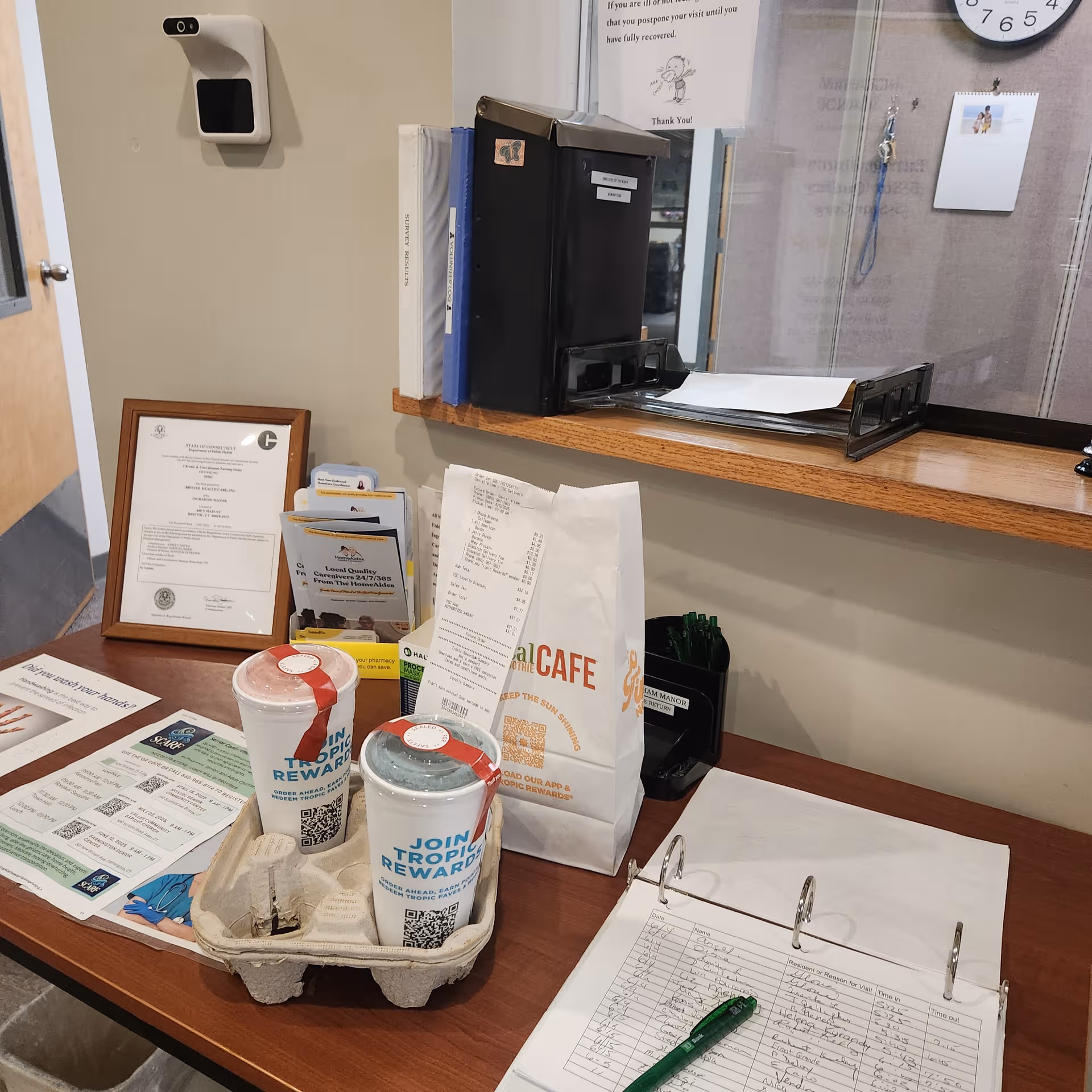 Reception counter at Ingraham Manor Nursing Home with papers, folders, cups, and a wall clock.