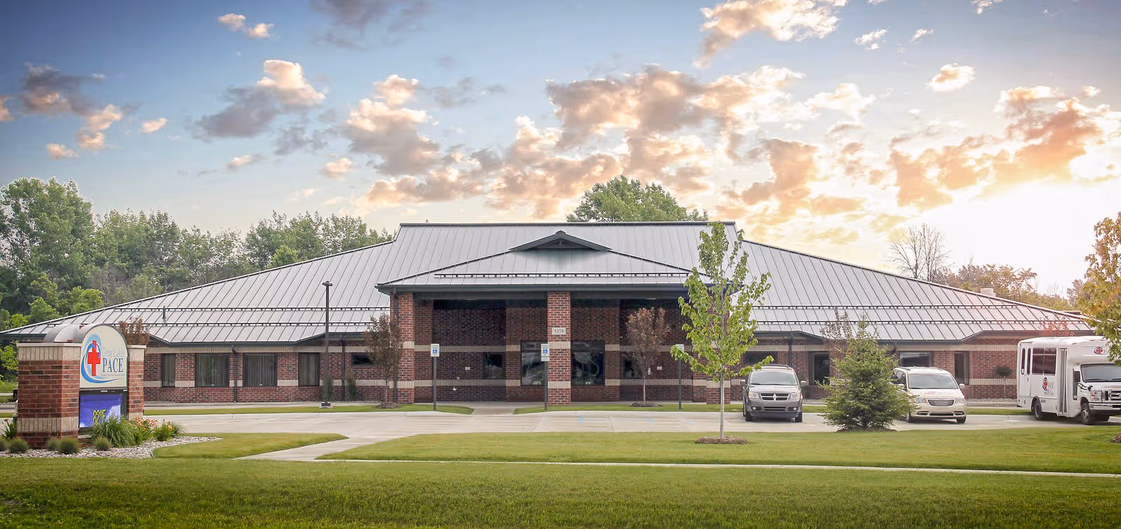 Single-story brick facility with a metal roof, parking lot, and buses outside.