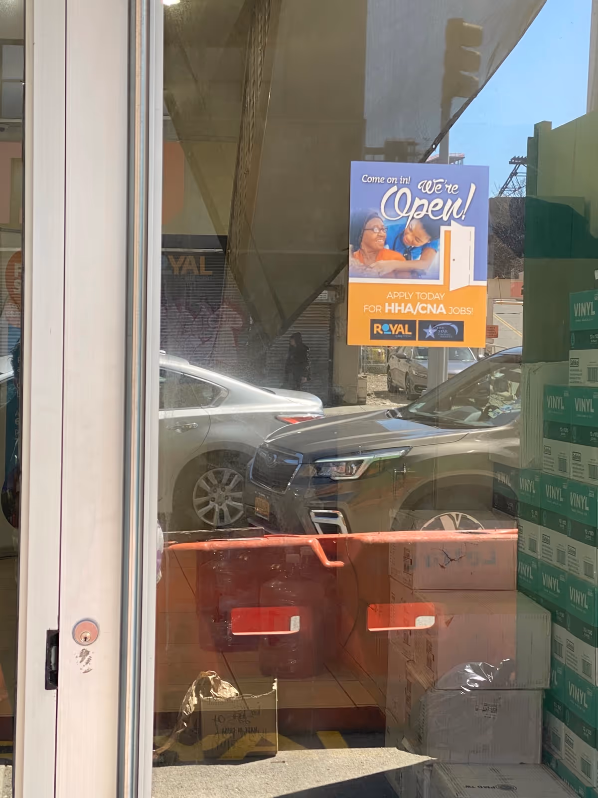 Glass storefront with an 'Open' sign, parked cars, and stacked boxes.