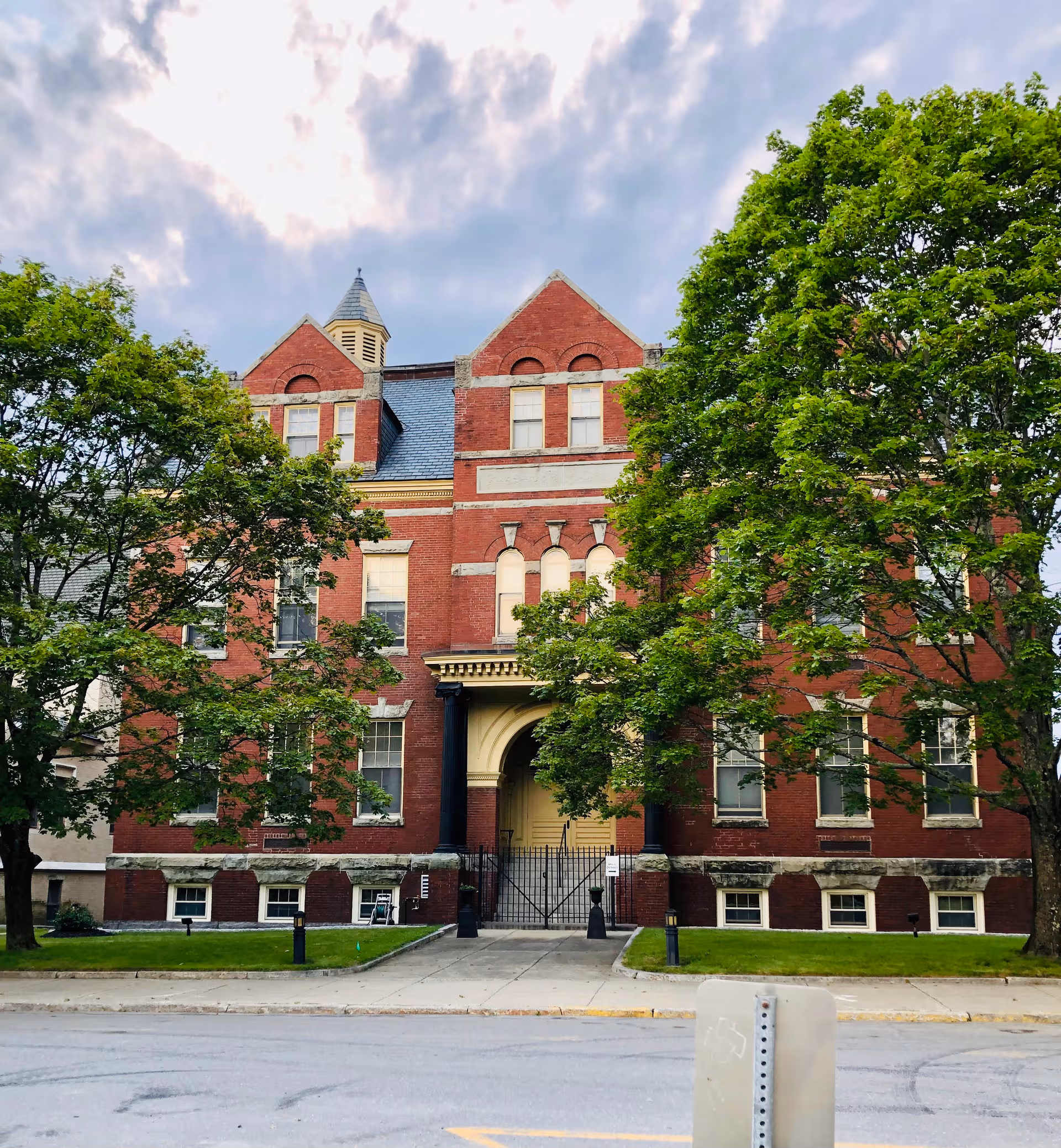 Red brick assisted-living building with arched entrance framed by tall trees.