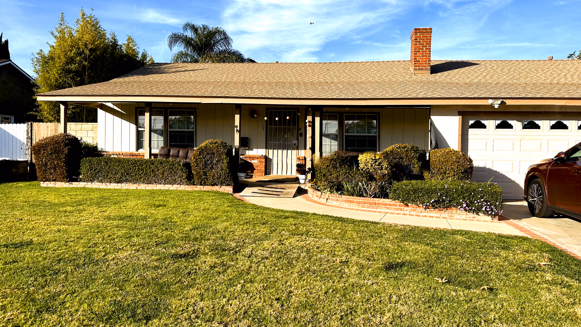 Single-story ranch-style house with a front lawn, trimmed shrubs, and an attached garage.