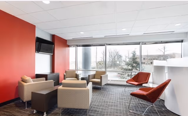 Modern lounge area inside a senior facility with red wall, seating, and large windows.