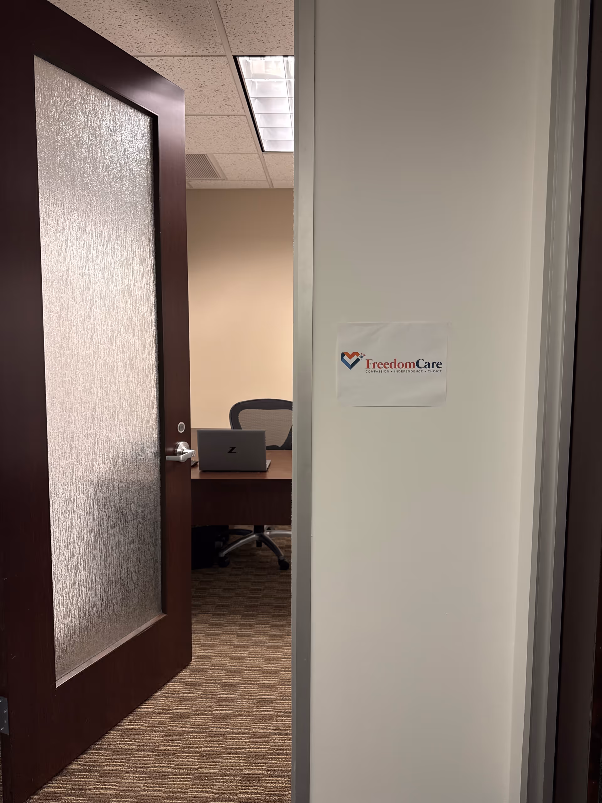 Open doorway reveals a small office with desk, laptop, chair, and FreedomCare sign.