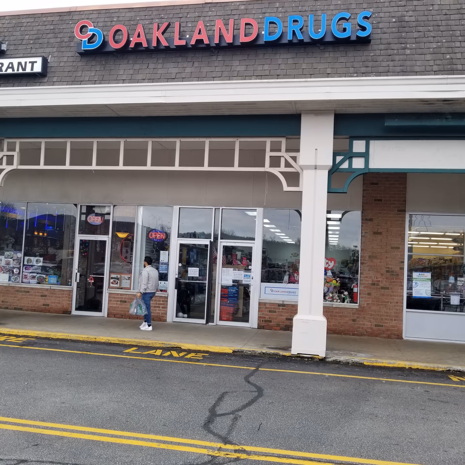 Exterior view of Oakland Drugs storefront with glass doors and a person walking by