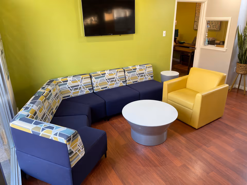 Bright lounge with blue patterned sectional, yellow armchair, and white round coffee table.