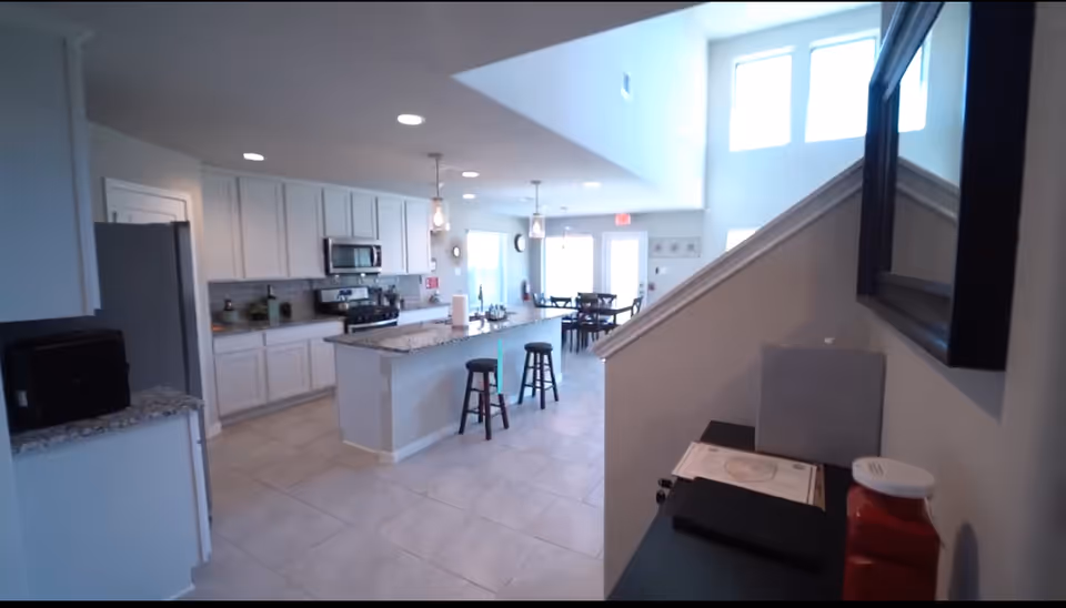 Open-concept kitchen and dining area with white cabinets, island, and bar stools.