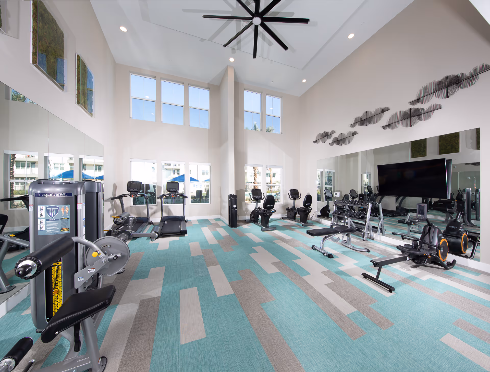 Bright senior living facility gym featuring cardio machines, weight equipment, mirrors, and large windows.
