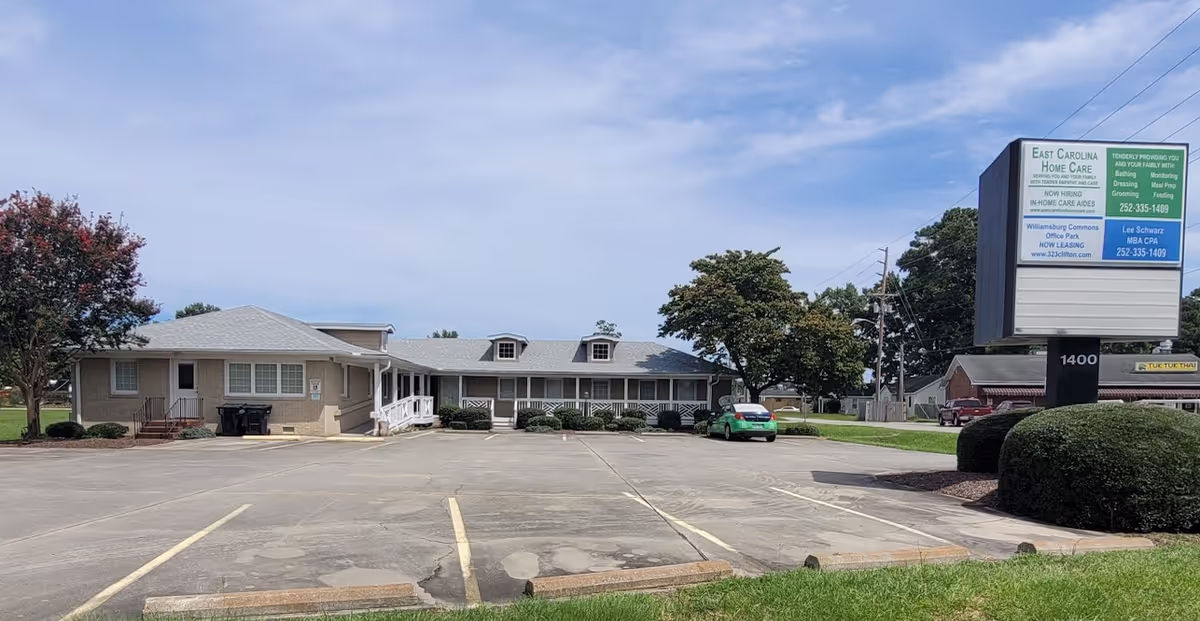 Single-story beige senior care building with parking lot and large sign in front.