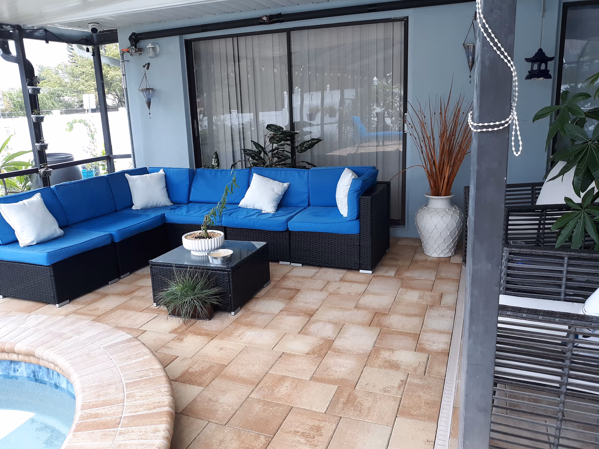 Outdoor patio with blue-cushioned sectional seating, glass table, and potted plants.