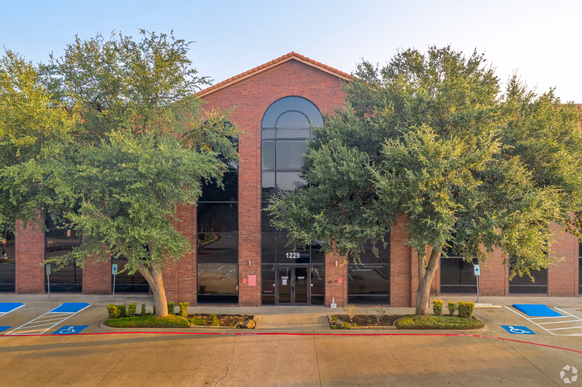 Brick building front with arched windows, trees, and handicap parking in foreground.