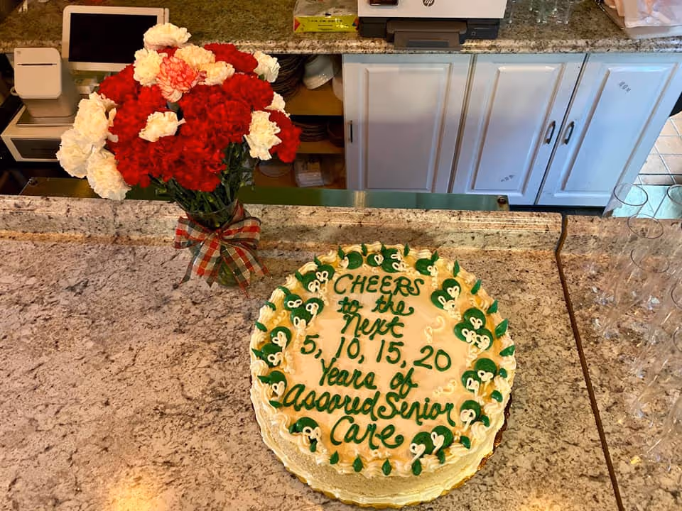 Cake with green icing sits on granite counter beside a red and white flower bouquet.