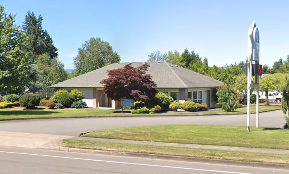 Single-story building with brick exterior, landscaped yard, and a curved driveway.