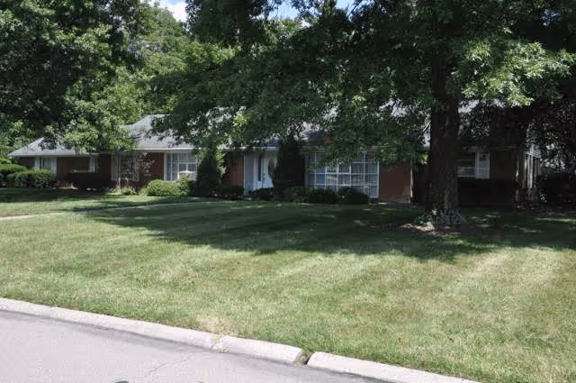 Single-story brick house with a large front lawn and mature trees.