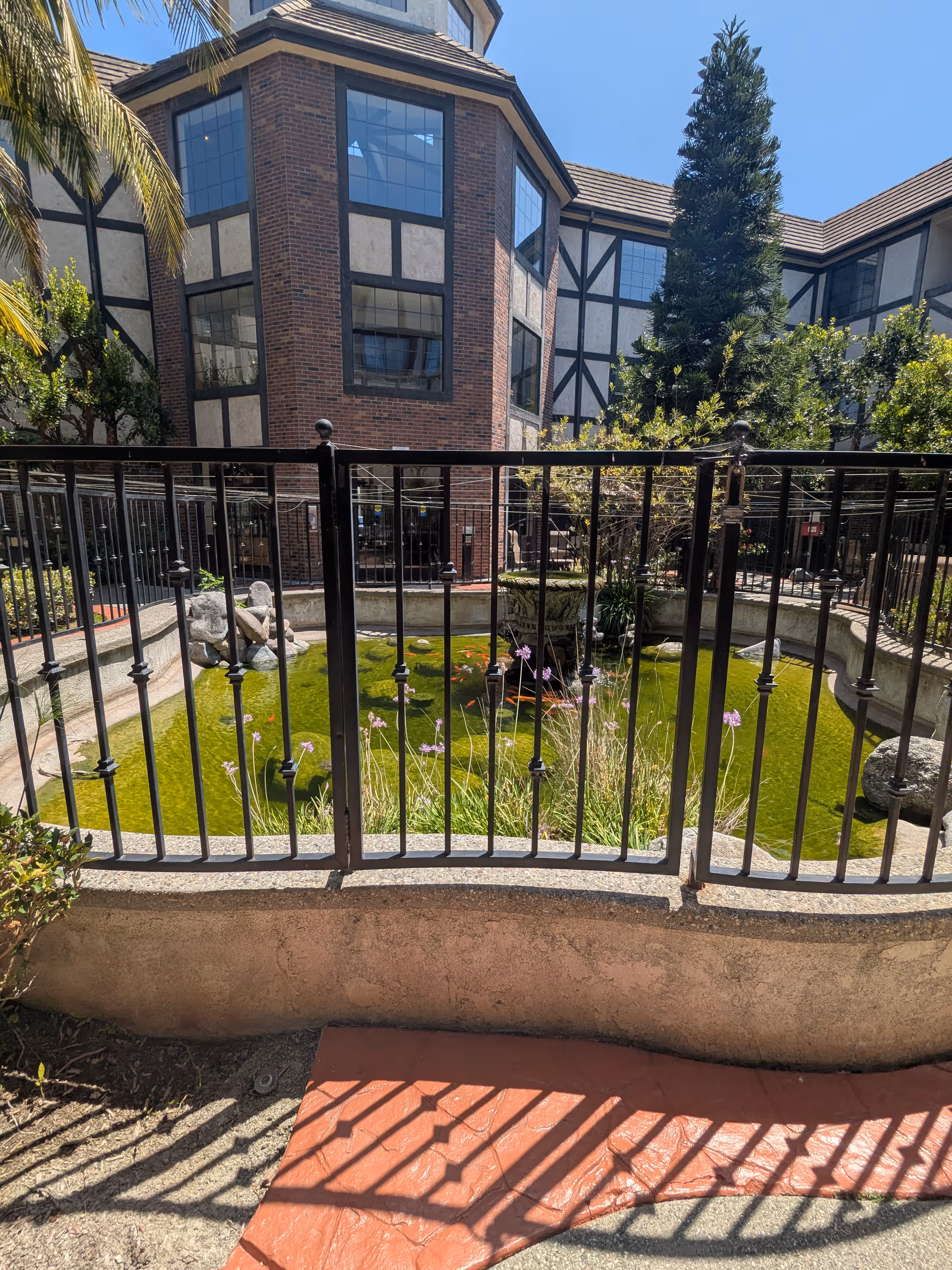 Exterior courtyard of a senior living campus featuring a pond, railing, and brick building facade.