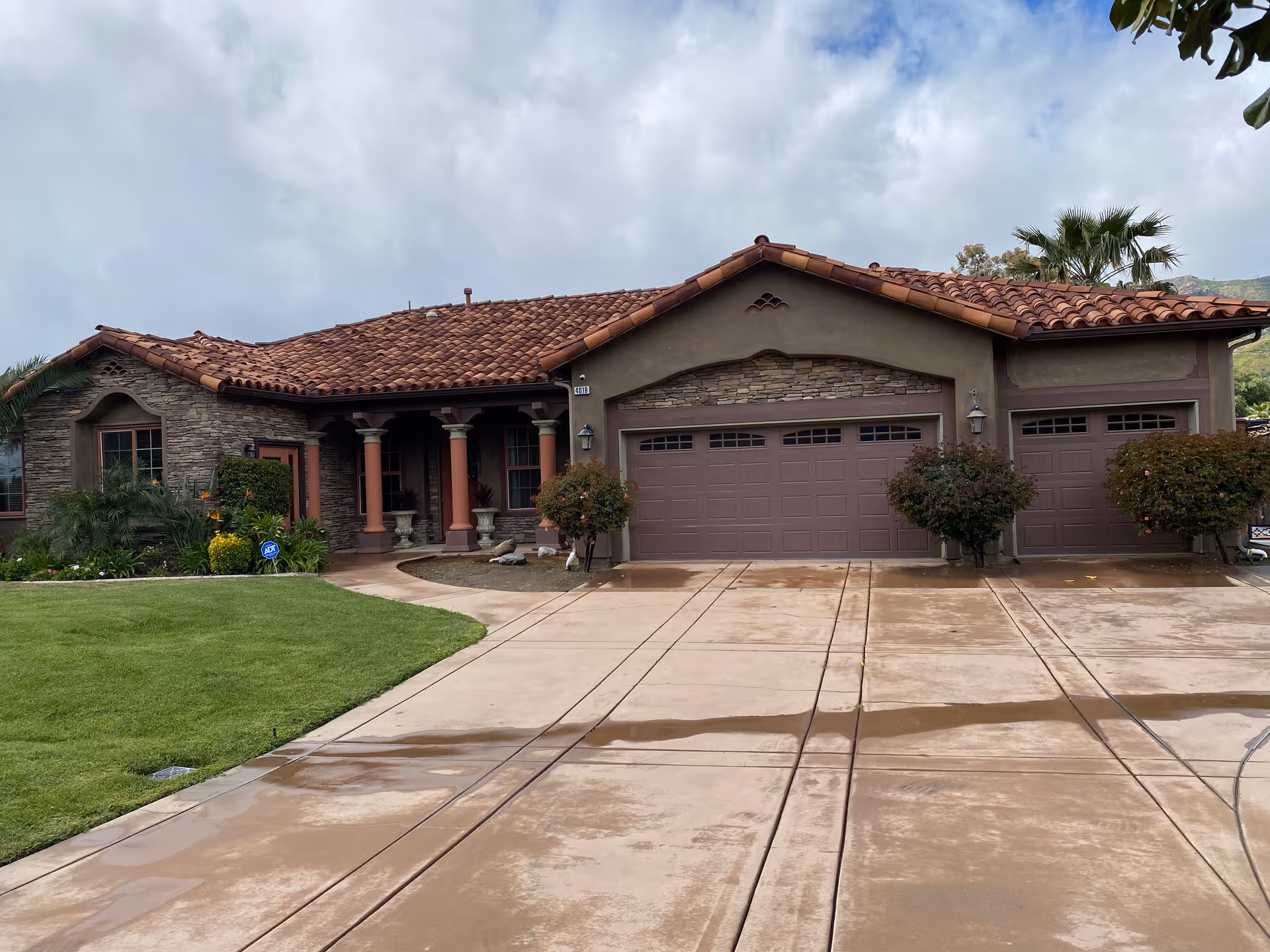Single-story tan stucco house with stone accents, red tile roof, and three-car garage.