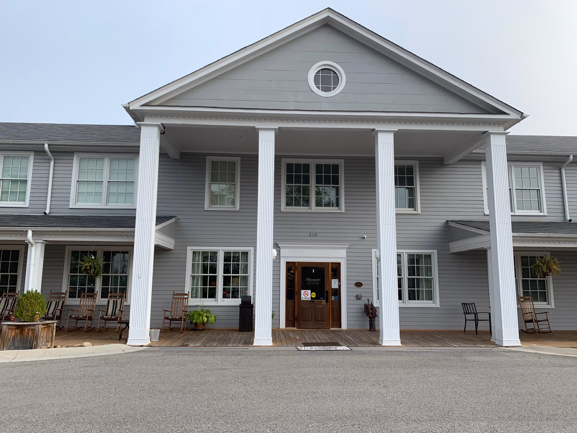 Gray senior living facility with tall white columns, double doors, and front porch seating.