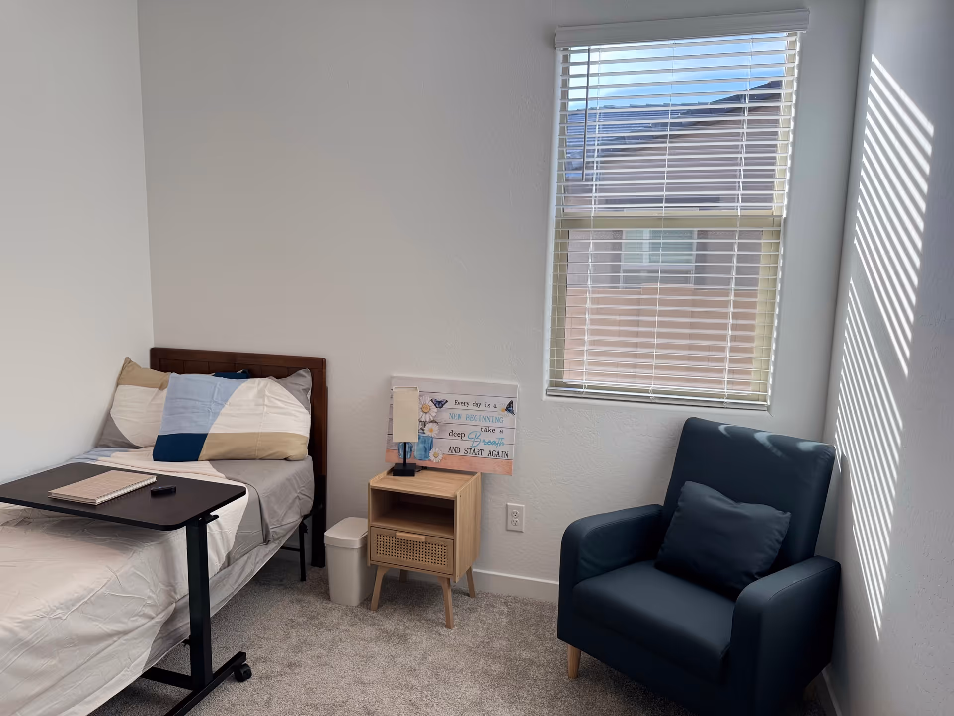 Compact bedroom in a senior living facility with a bed, nightstand, and blue armchair.