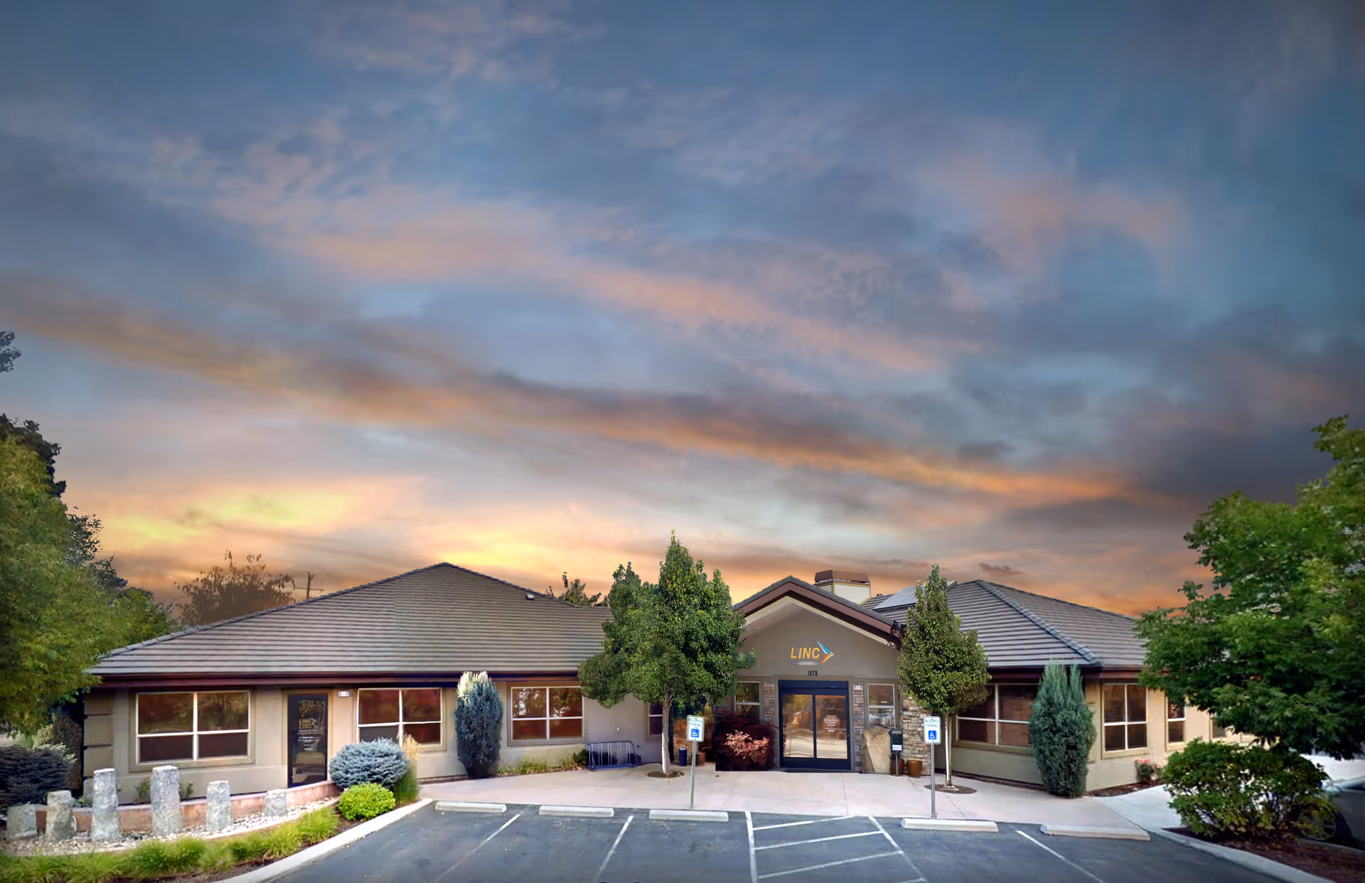 Front view of a senior living facility with parking, trees, and a sunset-lit sky.