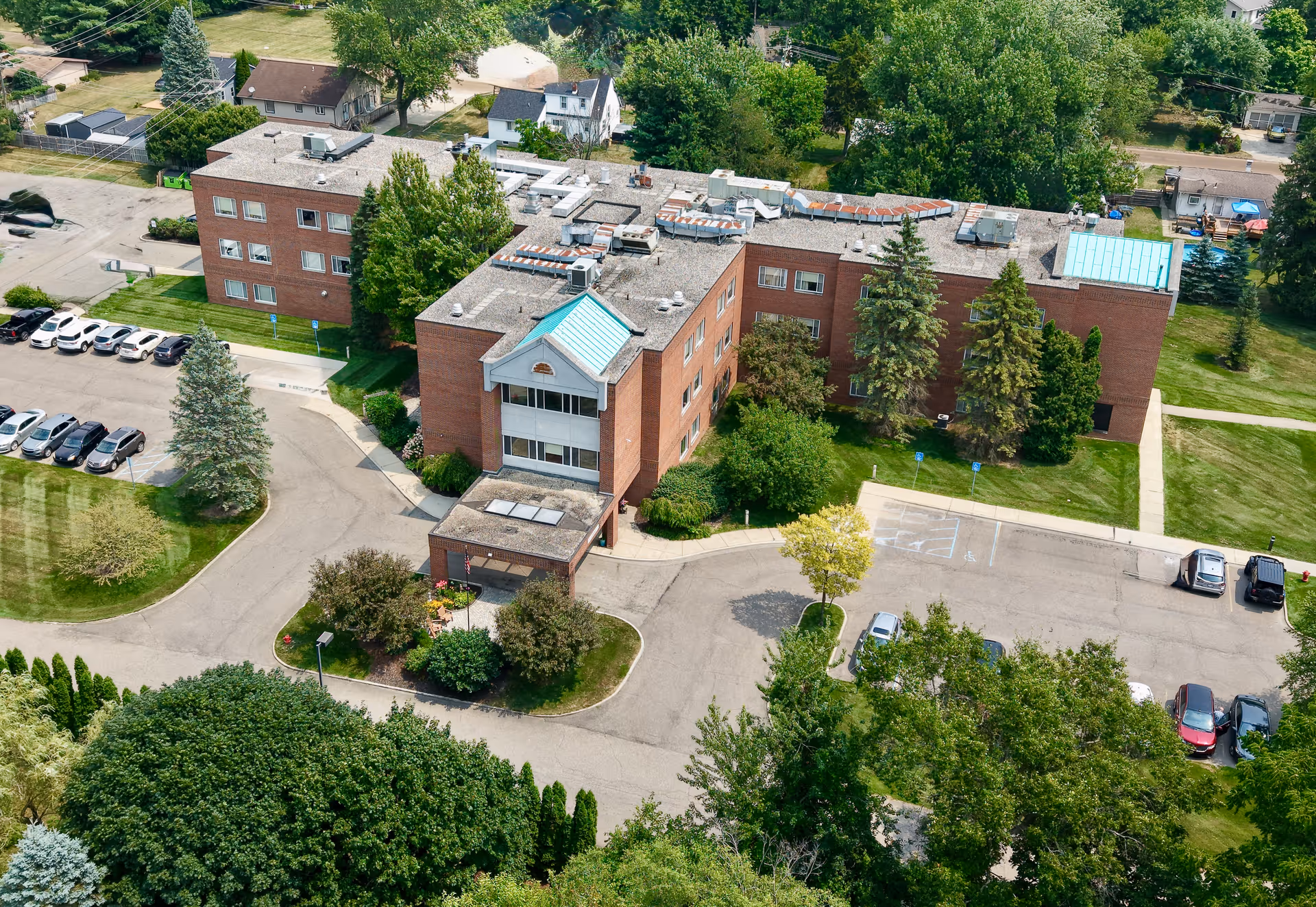 Aerial view of a brick senior living center with trees and parking.