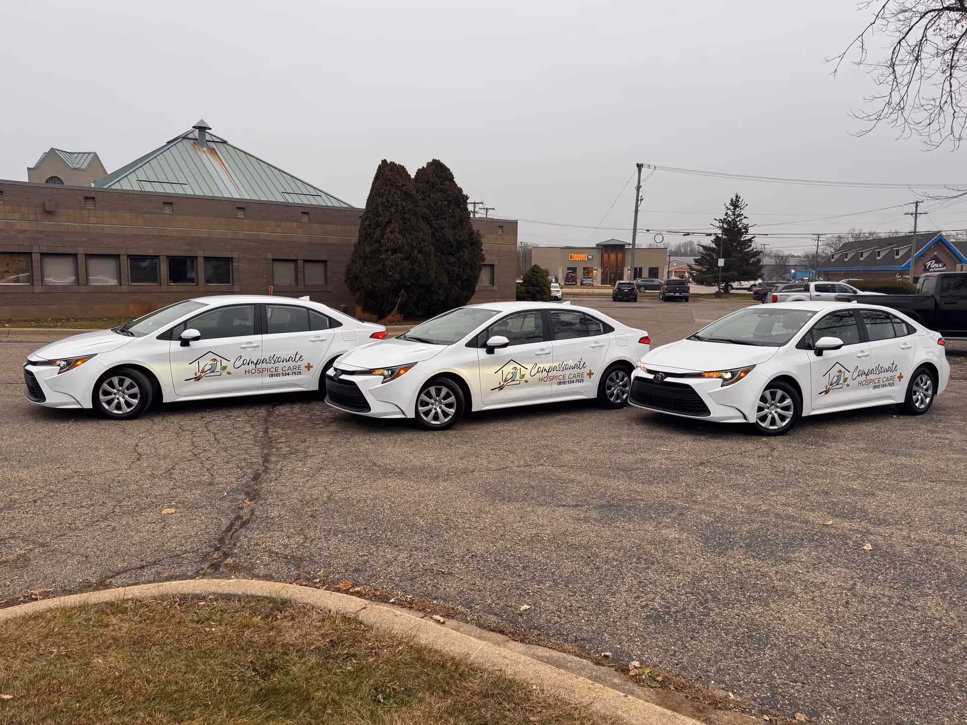 Three white Compassionate Hospice Care cars parked in a lot with a building behind.