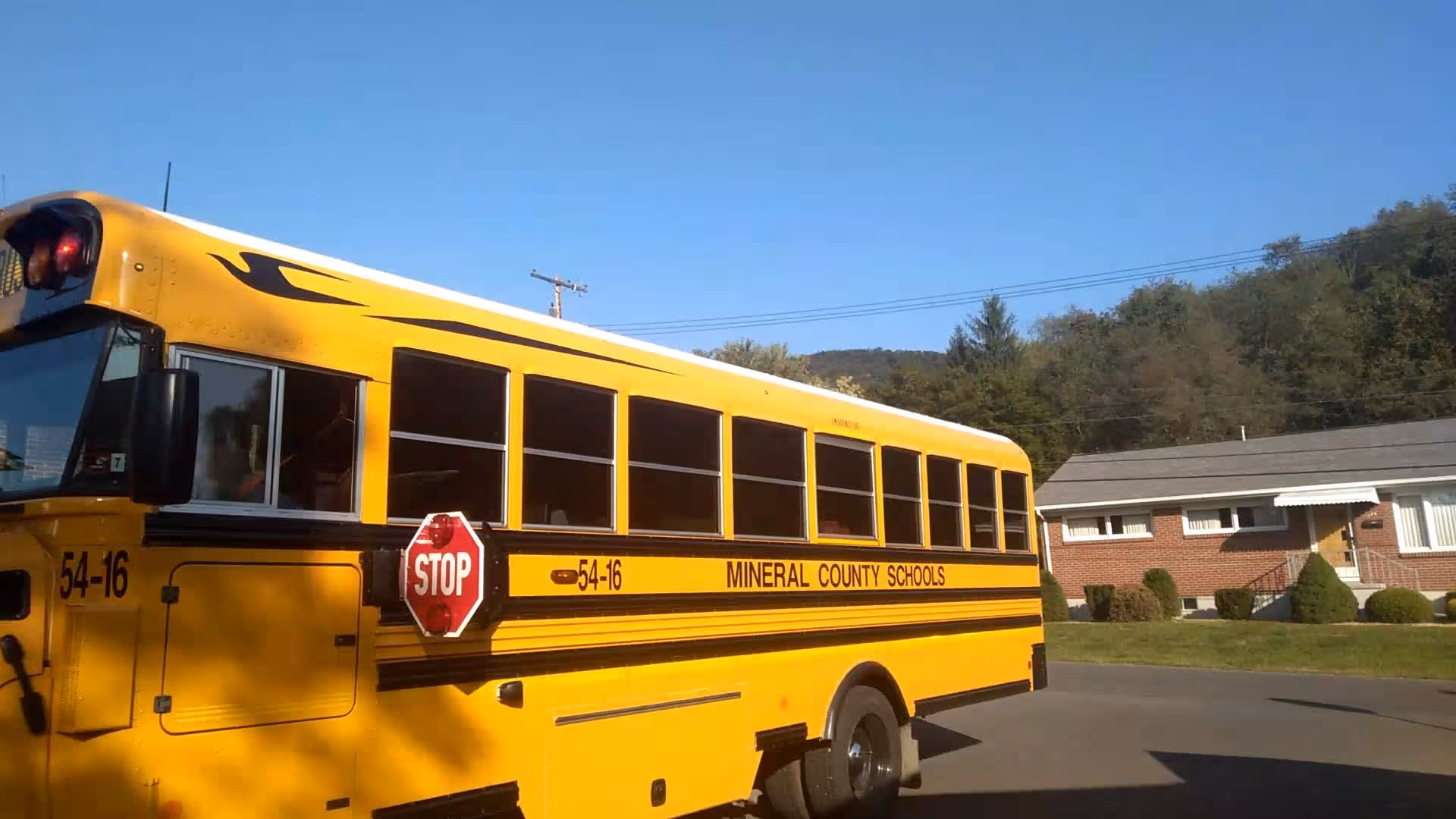 A yellow school bus parked on a street beside a brick building.