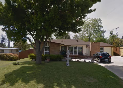 A single-story brick building with a driveway, front yard, and a parked car.