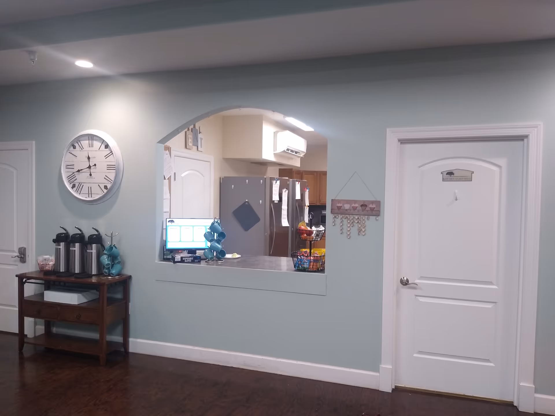 Light blue hallway with coffee station, large clock, and arched opening to the kitchen.