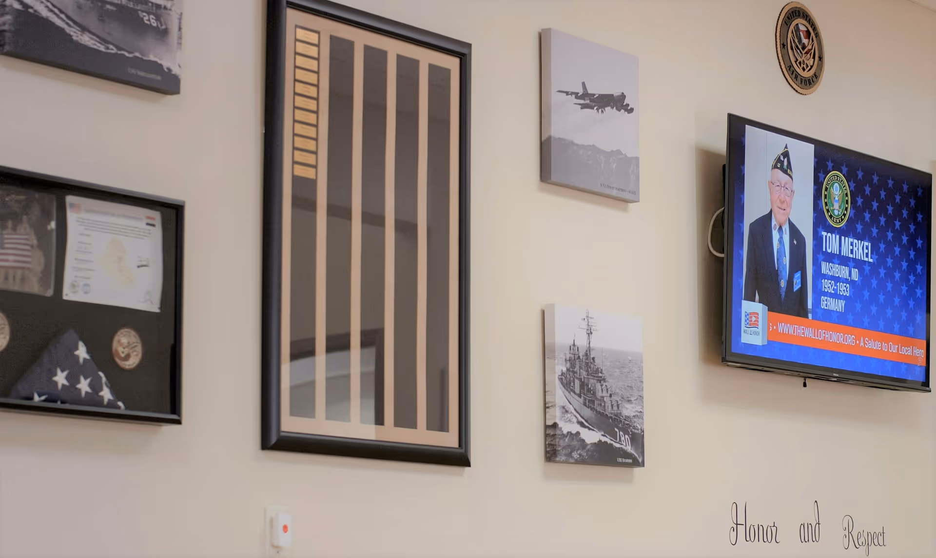 Interior wall displaying framed military memorabilia, photos, and a TV showing a veteran's profile.