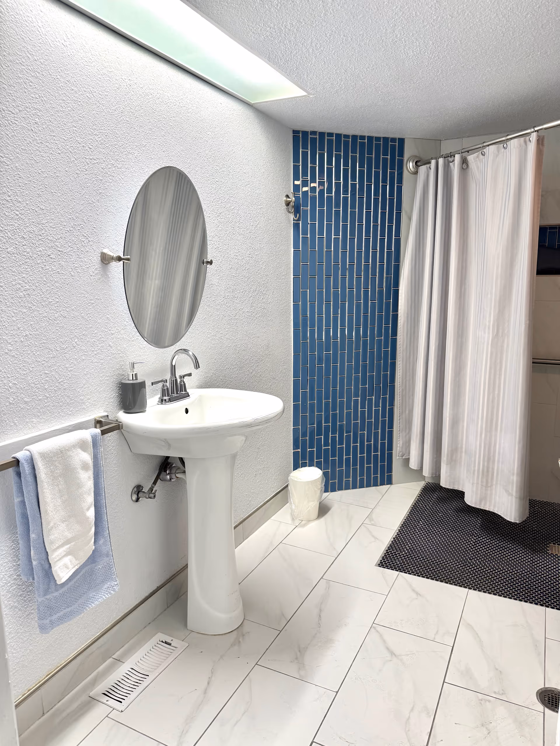 White-tiled bathroom in a senior home, with pedestal sink, blue tile wall, and shower curtain.