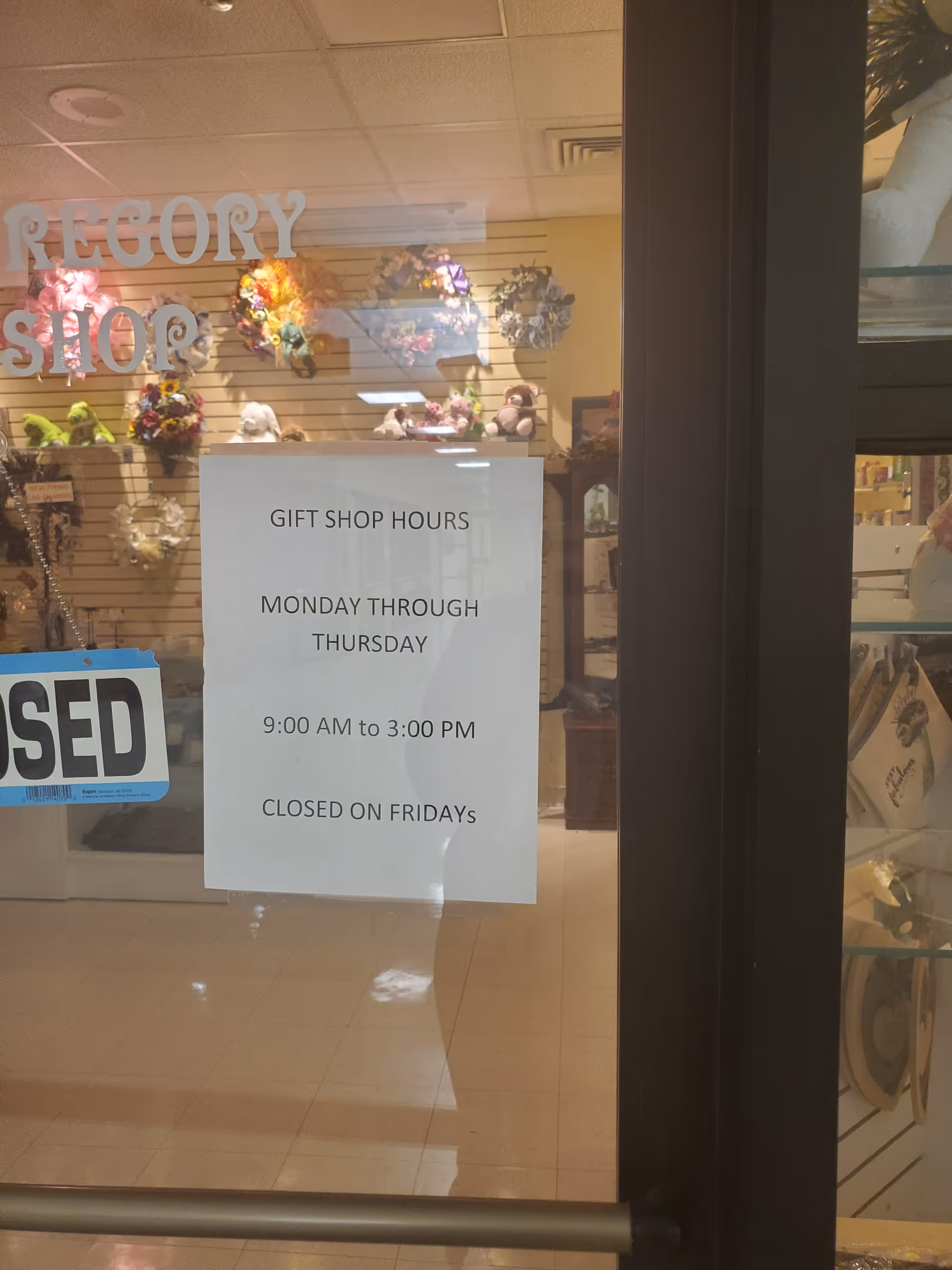 Hospital gift shop interior with displays and a posted hours sign on the glass door.