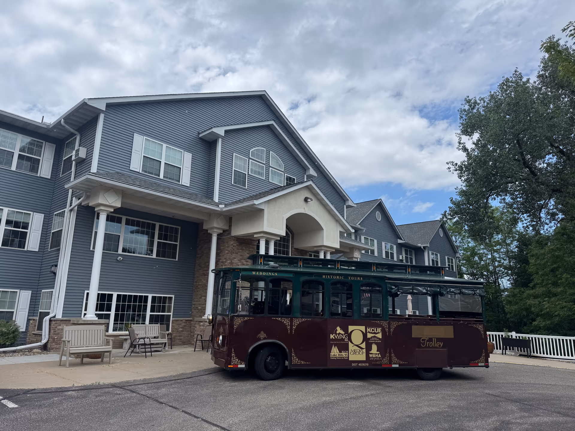 Blue multi-story senior living building with a maroon shuttle bus in front.