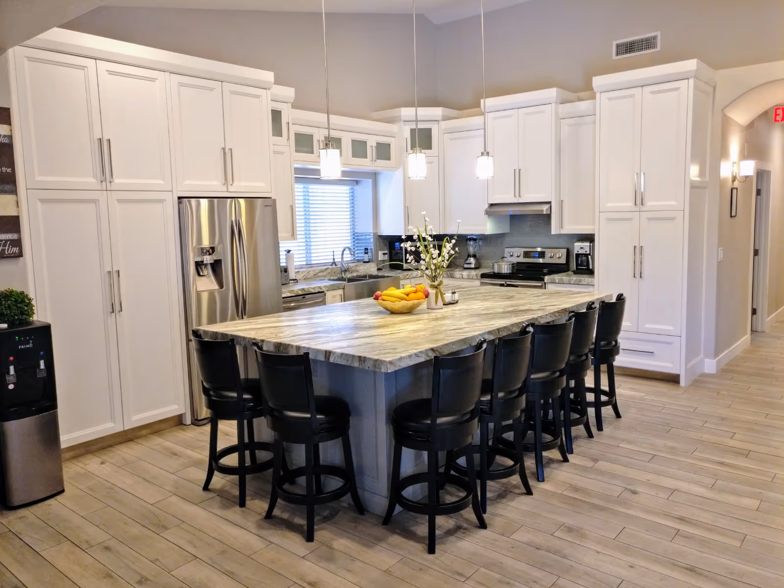 Bright white kitchen with marble island, pendant lights, and black stools in a senior living facility.