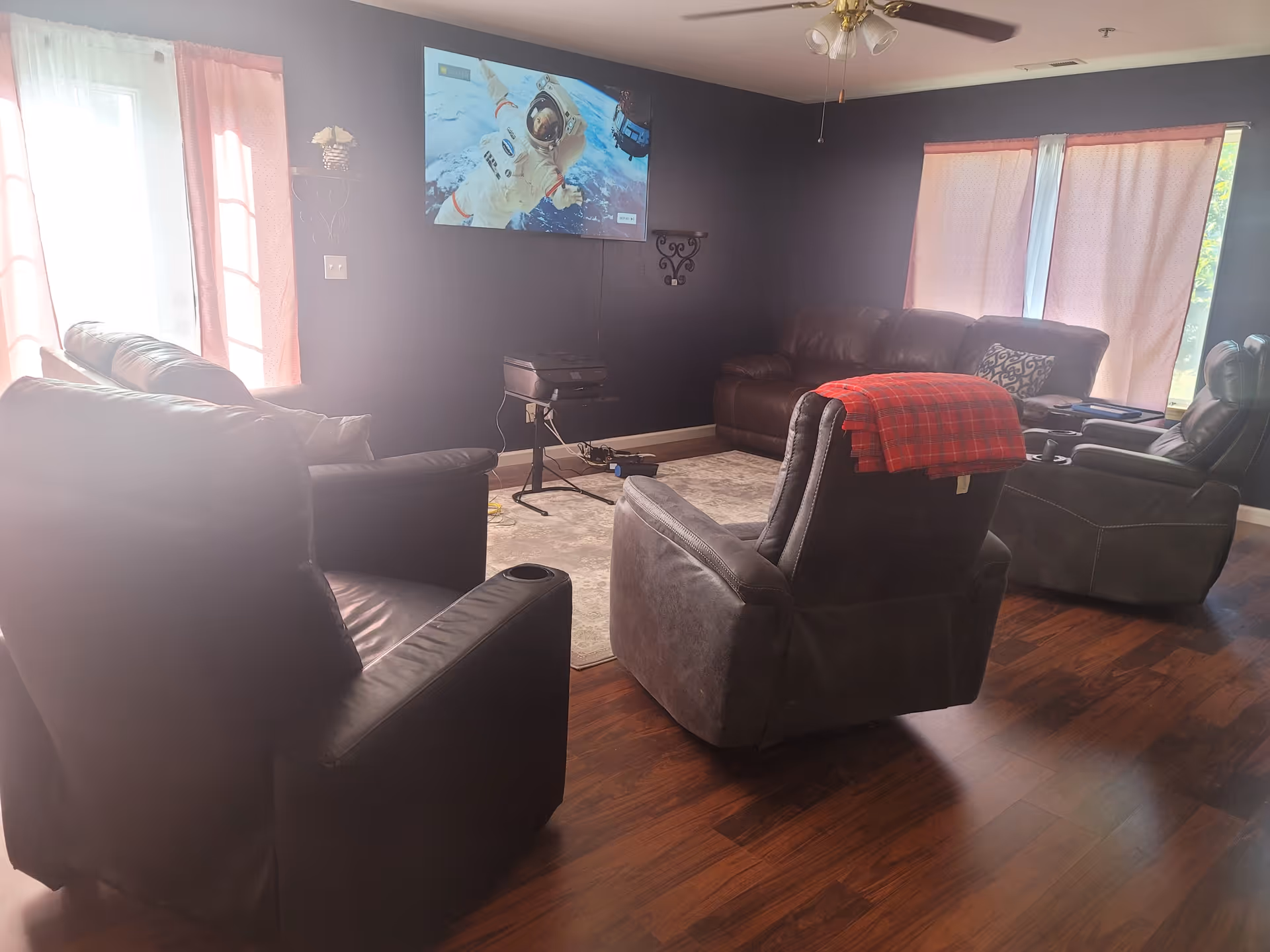 Living room with leather recliners, a wall-mounted TV, dark walls, and pink curtains.