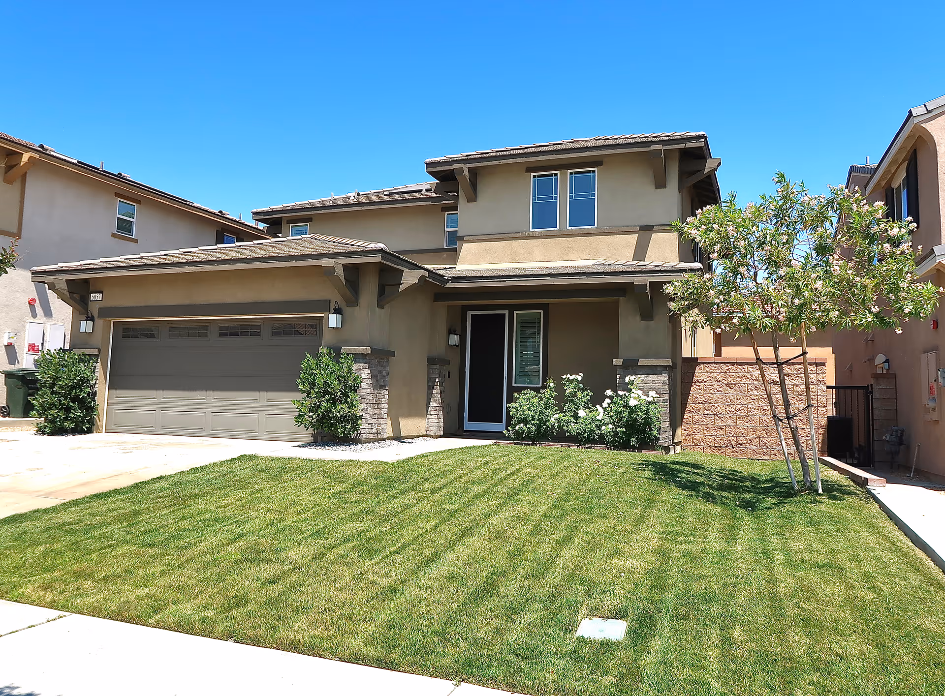 Front view of a two-story beige house with a two-car garage and a green lawn.